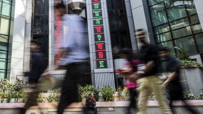 People walk past electronic boards displaying stock figures in the atrium of the National Stock Exchange of India, in Mumbai